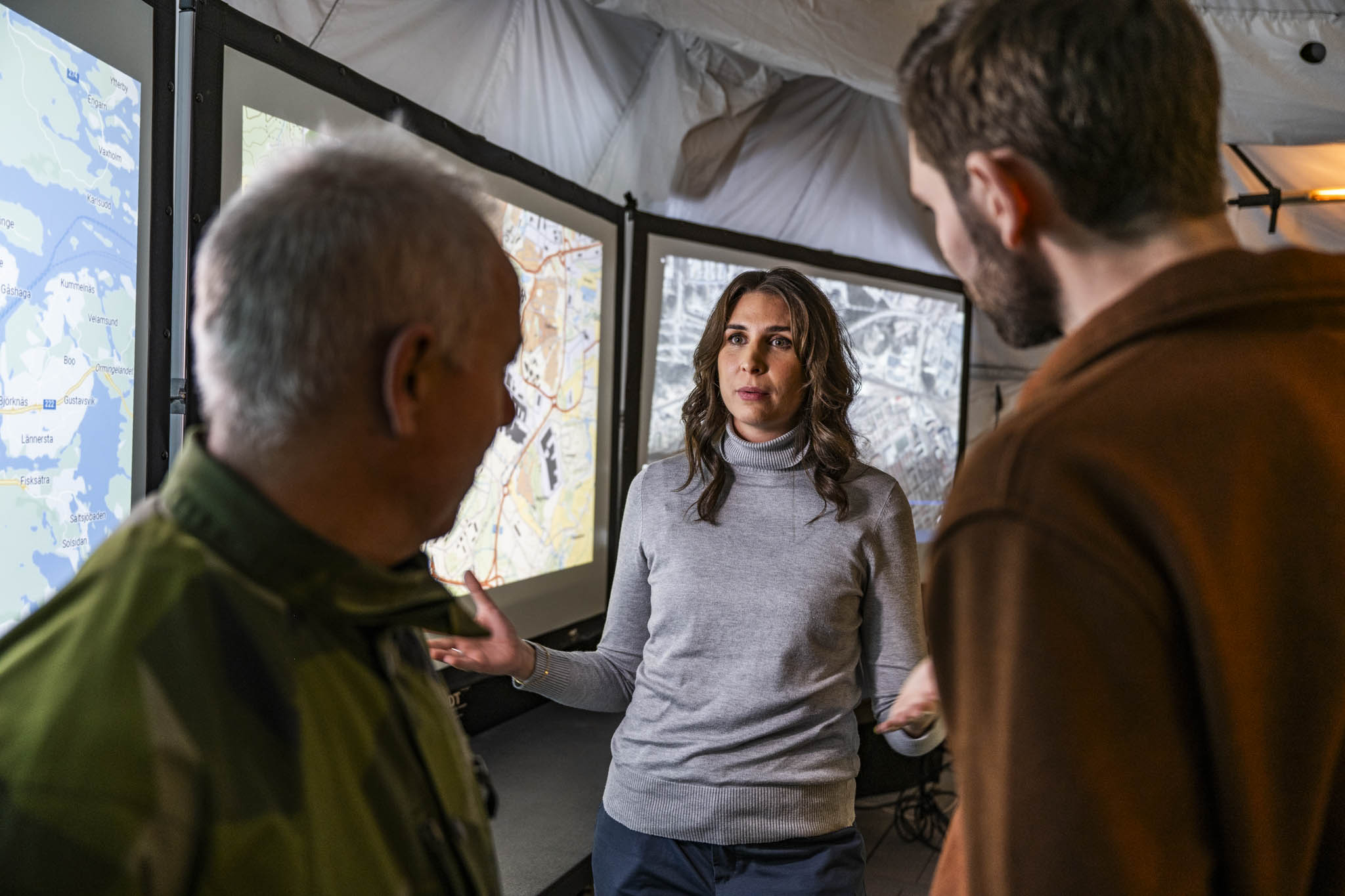 Two civilians and a military man discuss in front of digital maps at an exercise in Enköping.